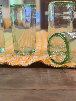 Four clear shot glasses with green rims on a patterned cloth