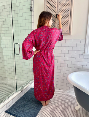 Woman in a pink floral robe standing in a bathroom with tiled walls and a bathtub.