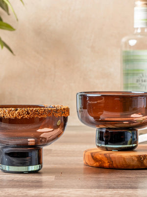 Two brown glasses on a wooden surface with a bottle and lime in the background.