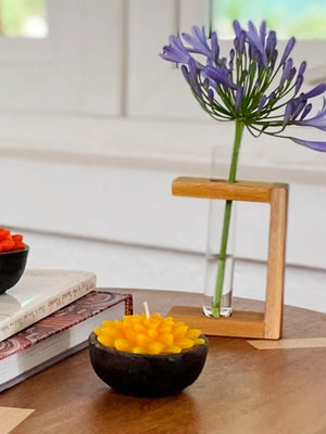 Decorative candles in black bowls with a purple flower in a glass vase on a wooden surface.
